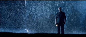 Movie still from “Adam's Apples” (2005), directed by Anders Thomas Jensen – A man holding a flashlight standing in the rain; Wide shot, Low angle