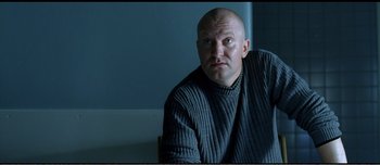 Movie still from “Adam's Apples” (2005), directed by Anders Thomas Jensen – A bald man in a sweater sitting on a chair; Close Up shot, Low angle