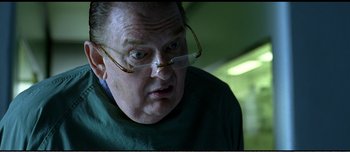 Movie still from “Adam's Apples” (2005), directed by Anders Thomas Jensen – An older man wearing glasses and a green shirt looking at the camera; Close Up shot, Over the shoulder angle