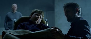 Movie still from “Adam's Apples” (2005), directed by Anders Thomas Jensen – A young boy laying in a chair next to an adult; Medium shot, Over the shoulder angle