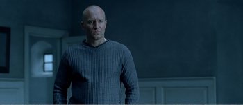 Movie still from “Adam's Apples” (2005), directed by Anders Thomas Jensen – A bald man in a sweater standing in front of a wall; Medium shot, Low angle