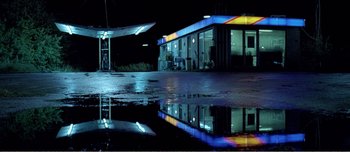 Movie still from “Adam's Apples” (2005), directed by Anders Thomas Jensen – A gas station at night reflecting in a pool of water; Extreme Wide shot, High angle
