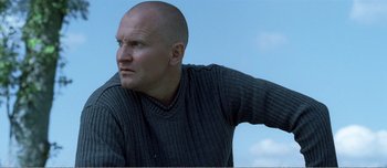 Movie still from “Adam's Apples” (2005), directed by Anders Thomas Jensen – A bald man in a gray sweater looks to his left; Close Up shot, Low angle