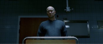 Movie still from “Adam's Apples” (2005), directed by Anders Thomas Jensen – A man standing in a kitchen wearing a sweater; Medium shot, Low angle