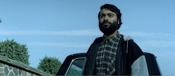 Movie still from “Adam's Apples” (2005), directed by Anders Thomas Jensen – A man standing next to a car with a beard; Close Up shot, Low angle