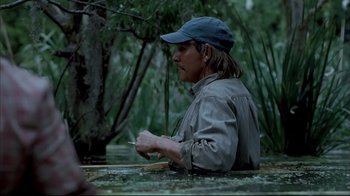 Movie still from “Adaptation.” (2002), directed by Spike Jonze – A man sitting in the water holding a fishing pole; Medium shot, Over the shoulder angle