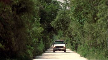 Movie still from “Adaptation.” (2002), directed by Spike Jonze – A car driving down a road surrounded by trees; Extreme Wide shot, High angle