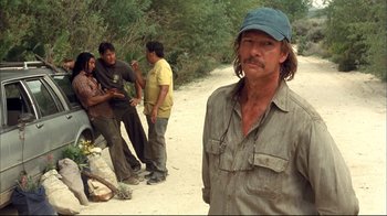 Movie still from “Adaptation.” (2002), directed by Spike Jonze – A man standing in front of a group of people on a dirt road; Medium shot, Over the shoulder angle