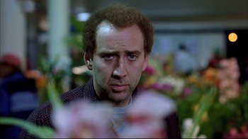 Movie still from “Adaptation.” (2002), directed by Spike Jonze – Nicolas cage looking at the camera with flowers in the background; Close Up shot, Over the shoulder angle