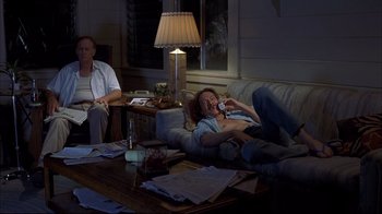 Movie still from “Adaptation.” (2002), directed by Spike Jonze – A man sitting on top of a couch next to a table; Wide shot, High angle