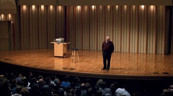 Movie still from “Adaptation.” (2002), directed by Spike Jonze – A man standing in front of an audience on a stage; Wide shot, High angle