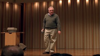 Movie still from “Adaptation.” (2002), directed by Spike Jonze – An older man standing on a stage holding a microphone; Medium shot, Over the shoulder angle