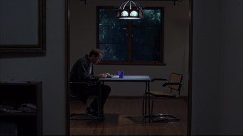 Movie still from “Adaptation.” (2002), directed by Spike Jonze – A man sitting at a table in front of a window; Wide shot, High angle