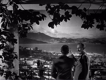 Movie still from “Address Unknown” (1944), directed by William Cameron Menzies – Two men standing on a balcony looking at a lake; Medium shot, Over the shoulder angle