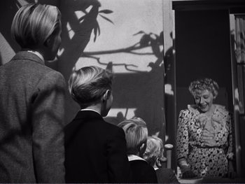 Movie still from “Address Unknown” (1944), directed by William Cameron Menzies – A group of people standing next to each other in a room; Medium shot, Over the shoulder angle