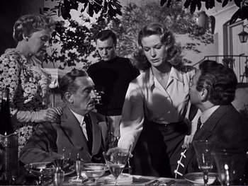 Movie still from “Address Unknown” (1944), directed by William Cameron Menzies – An old black and white photo of a group of people sitting at a dinner table; Medium shot, Over the shoulder angle
