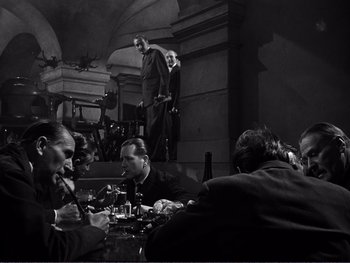 Movie still from “Address Unknown” (1944), directed by William Cameron Menzies – A black and white photo of a group of people sitting at a table; Wide shot, High angle