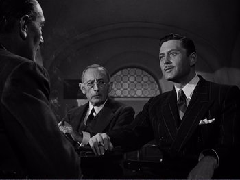 Movie still from “Address Unknown” (1944), directed by William Cameron Menzies – A group of men standing next to each other in a room; Medium shot, Over the shoulder angle