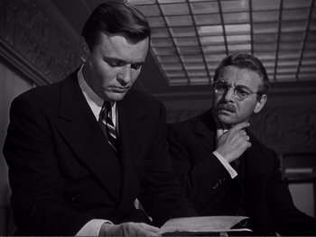 Movie still from “Address Unknown” (1944), directed by William Cameron Menzies – Two men in suits looking at a piece of paper; Medium shot, Over the shoulder angle