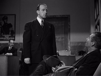 Movie still from “Address Unknown” (1944), directed by William Cameron Menzies – A man in a suit standing in front of two other men; Medium shot, Low angle