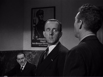 Movie still from “Address Unknown” (1944), directed by William Cameron Menzies – A man in a suit and tie standing next to another man in a suit and tie; Medium shot, Low angle