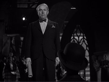 Movie still from “Address Unknown” (1944), directed by William Cameron Menzies – A man in a suit and bow tie standing in front of another man in a suit and bow tie; Medium shot, Low angle