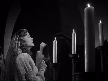 Movie still from “Address Unknown” (1944), directed by William Cameron Menzies – A woman is praying in front of some candles; Medium shot, Low angle