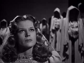 Movie still from “Address Unknown” (1944), directed by William Cameron Menzies – A black and white photo of a woman in front of a group of people; Close Up shot, Low angle