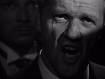 Movie still from “Address Unknown” (1944), directed by William Cameron Menzies – Black and white photograph of a man in a suit and tie; Close Up shot, Low angle