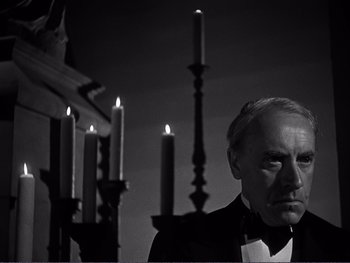Movie still from “Address Unknown” (1944), directed by William Cameron Menzies – A black and white photo of a man in front of a bunch of lit candles; Close Up shot, Low angle