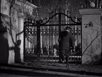 Movie still from “Address Unknown” (1944), directed by William Cameron Menzies – A man walking in front of an iron gate at night; Wide shot, Low angle