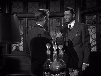 Movie still from “Address Unknown” (1944), directed by William Cameron Menzies – Two men in suits are standing in front of a bar; Medium shot, Over the shoulder angle
