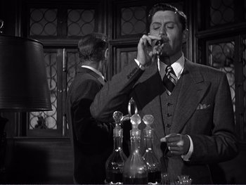 Movie still from “Address Unknown” (1944), directed by William Cameron Menzies – A man in a suit and tie is drinking a drink; Medium shot, Low angle