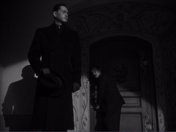 Movie still from “Address Unknown” (1944), directed by William Cameron Menzies – A man in a suit and a hat standing next to another man in a suit and a hat; Medium shot, Low angle