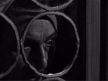 Movie still from “Address Unknown” (1944), directed by William Cameron Menzies – A man looking through a bunch of metal pipes; Close Up shot, High angle