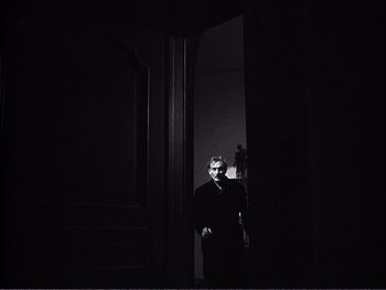 Movie still from “Address Unknown” (1944), directed by William Cameron Menzies – A man standing in a dark room in front of an open door; Medium shot, Low angle