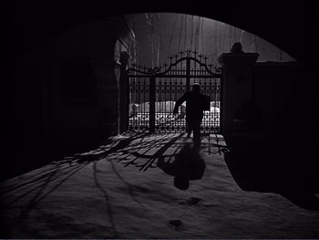 Movie still from “Address Unknown” (1944), directed by William Cameron Menzies – A person walking in the snow near an iron gate; Wide shot, Low angle