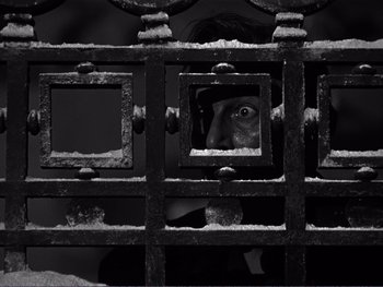 Movie still from “Address Unknown” (1944), directed by William Cameron Menzies – A person looking through a metal gate; Close Up shot, High angle