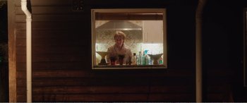 Movie still from “Adult Life Skills” (2016), directed by Rachel Tunnard – A woman standing at a counter in a kitchen looking out of a window; Medium shot, Low angle