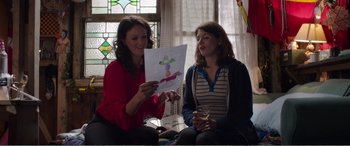 Movie still from “Adult Life Skills” (2016), directed by Rachel Tunnard – Two women sitting in front of each other holding a drawing; Medium shot, Over the shoulder angle