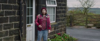 Movie still from “Adult Life Skills” (2016), directed by Rachel Tunnard – A person standing in front of a brick building; Wide shot, High angle