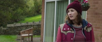 Movie still from “Adult Life Skills” (2016), directed by Rachel Tunnard – A woman wearing a hat standing in front of a building; Medium shot, Over the shoulder angle
