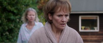 Movie still from “Adult Life Skills” (2016), directed by Rachel Tunnard – A woman in a bathrobe is looking at the camera while another woman looks on; Close Up shot, Over the shoulder angle