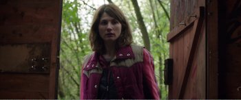 Movie still from “Adult Life Skills” (2016), directed by Rachel Tunnard – A woman standing in the woods wearing a pink jacket; Medium shot, Over the shoulder angle