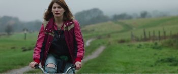 Movie still from “Adult Life Skills” (2016), directed by Rachel Tunnard – A woman riding a bike on a lush green field; Medium shot, High angle