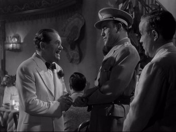Movie still from “Affair in Trinidad” (1952), directed by Vincent Sherman – A man in a white suit shaking hands with another man in a military uniform; Medium shot, Over the shoulder angle