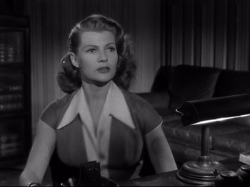 Movie still from “Affair in Trinidad” (1952), directed by Vincent Sherman – A black and white photo of a woman sitting at a table; Medium shot, Low angle