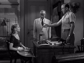 Movie still from “Affair in Trinidad” (1952), directed by Vincent Sherman – Two men and a woman are standing at a desk; Medium shot, Over the shoulder angle