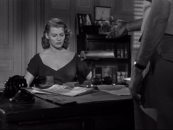 Movie still from “Affair in Trinidad” (1952), directed by Vincent Sherman – A woman sitting at a desk in front of a man; Medium shot, Over the shoulder angle
