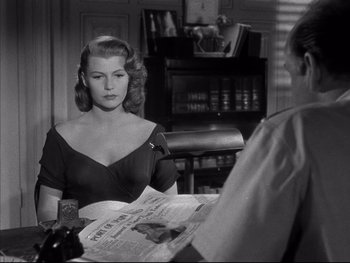 Movie still from “Affair in Trinidad” (1952), directed by Vincent Sherman – A woman sitting at a table with a newspaper; Medium shot, Over the shoulder angle